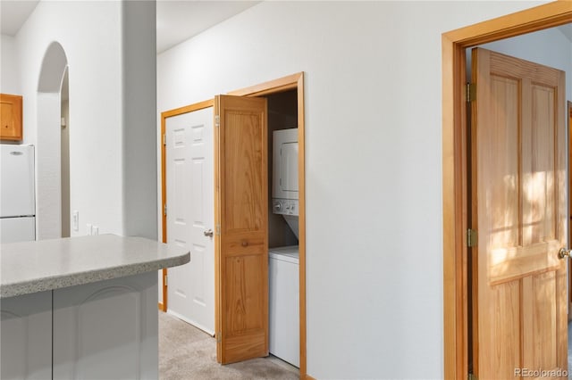 corridor with arched walkways, stacked washer / drying machine, and light colored carpet