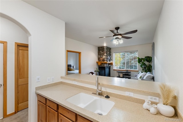 kitchen featuring arched walkways, a ceiling fan, brown cabinets, open floor plan, and a sink