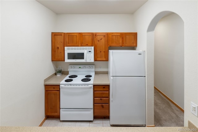 kitchen with light tile patterned floors, light countertops, brown cabinetry, white appliances, and baseboards