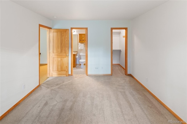 unfurnished bedroom with baseboards, a closet, a walk in closet, carpet, and ensuite bath