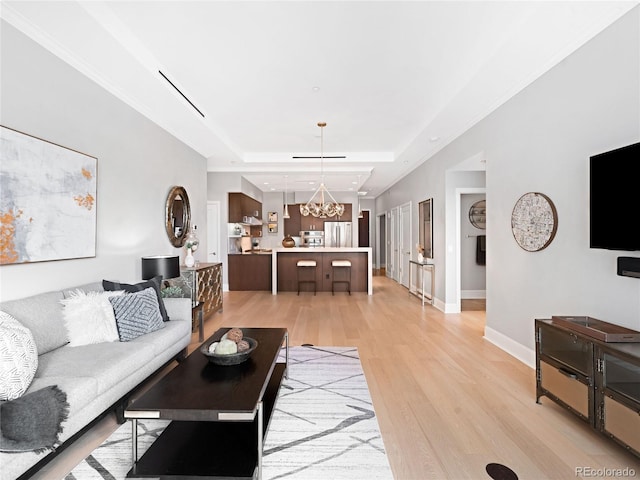 living room with a raised ceiling, a chandelier, and light hardwood / wood-style flooring