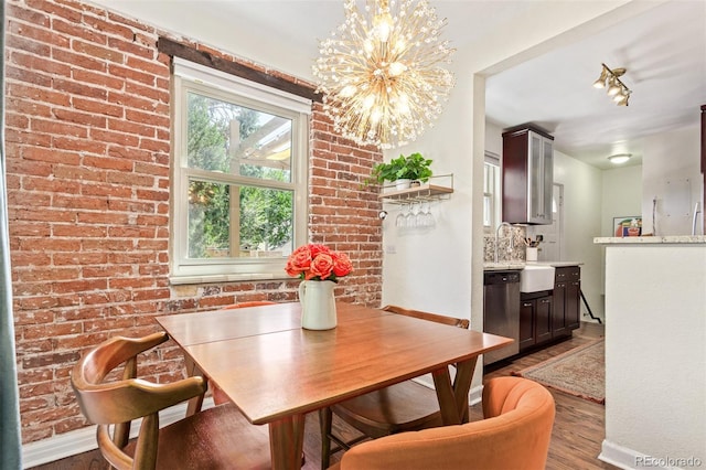 dining space with a notable chandelier, sink, wood-type flooring, and brick wall