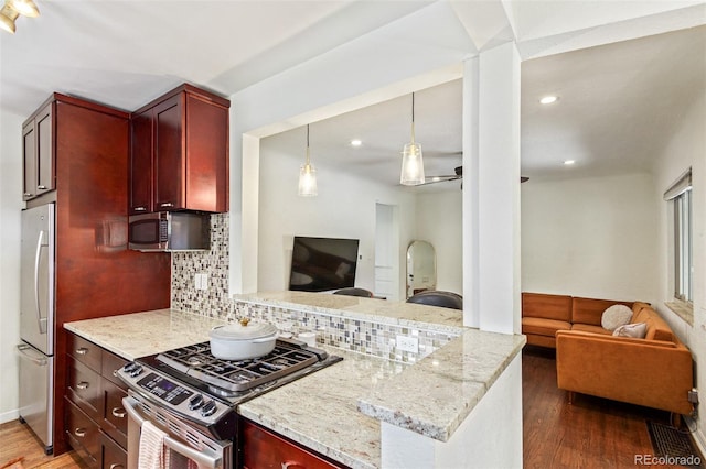 kitchen featuring appliances with stainless steel finishes, hanging light fixtures, backsplash, light stone counters, and hardwood / wood-style floors