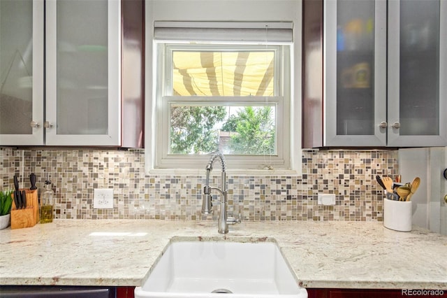 kitchen featuring decorative backsplash, sink, and light stone countertops