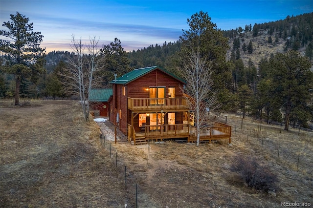 back of house at dusk featuring a wooded view and a deck