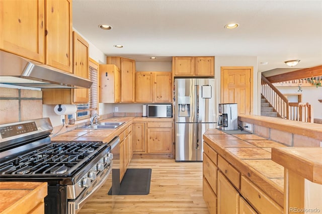 kitchen featuring under cabinet range hood, appliances with stainless steel finishes, tile counters, and a sink