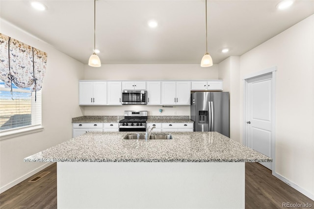 kitchen featuring appliances with stainless steel finishes, an island with sink, decorative light fixtures, white cabinets, and dark wood-type flooring