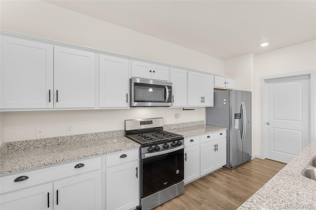 kitchen with white cabinets, light stone counters, stainless steel appliances, and light wood-type flooring