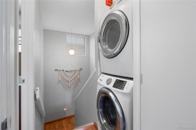 laundry area featuring a healthy amount of sunlight, stacked washer and clothes dryer, and wood-type flooring