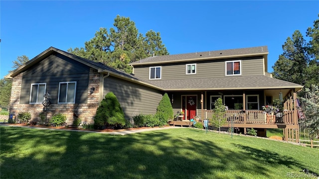 view of front facade with a front yard, a deck, stone siding, and roof with shingles