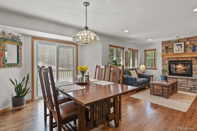 dining room featuring wood finished floors, a chandelier, recessed lighting, a stone fireplace, and baseboards