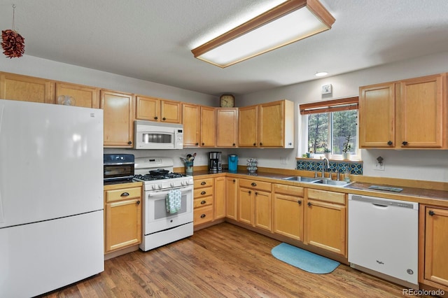 kitchen with white appliances, a sink, light wood-style floors, and light brown cabinets