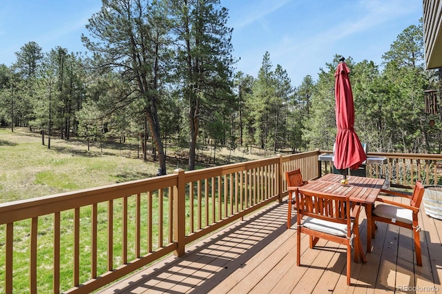 wooden terrace featuring outdoor dining space, a lawn, and view of wooded area