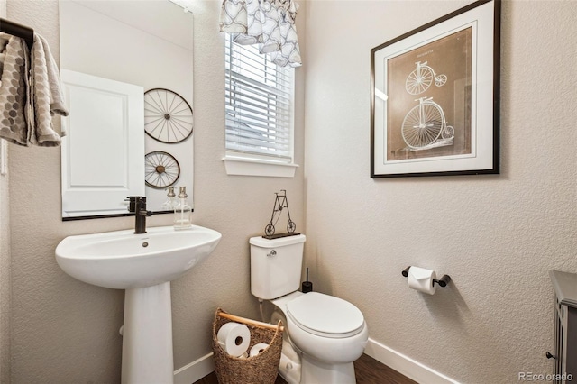 bathroom with toilet, baseboards, wood finished floors, and a textured wall