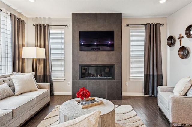 living room with dark wood-style flooring, a tile fireplace, and baseboards