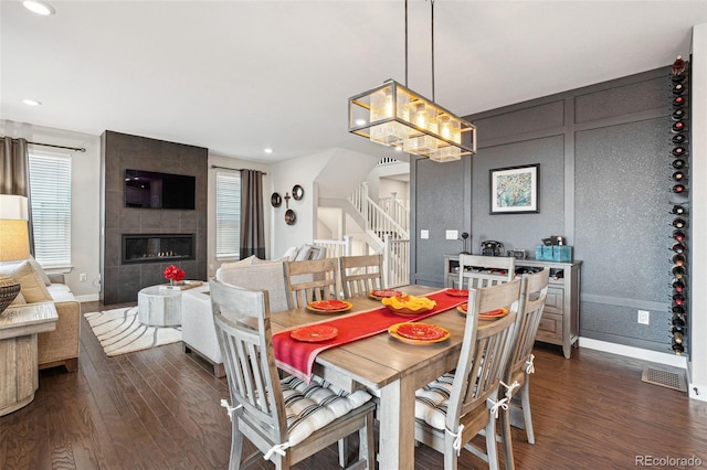 dining space with dark wood-type flooring, visible vents, a fireplace, and stairway