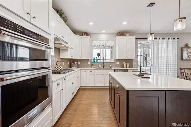 kitchen with white cabinets, stainless steel appliances, light countertops, under cabinet range hood, and a sink