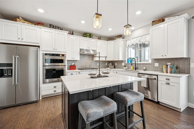 kitchen with under cabinet range hood, white cabinetry, a kitchen breakfast bar, appliances with stainless steel finishes, and dark wood finished floors