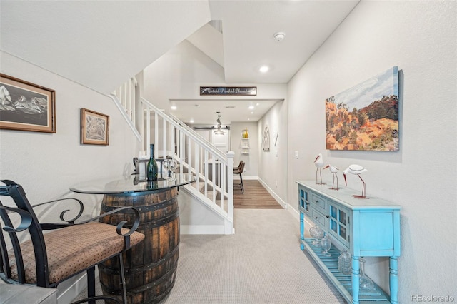 hall featuring light carpet, stairway, and baseboards