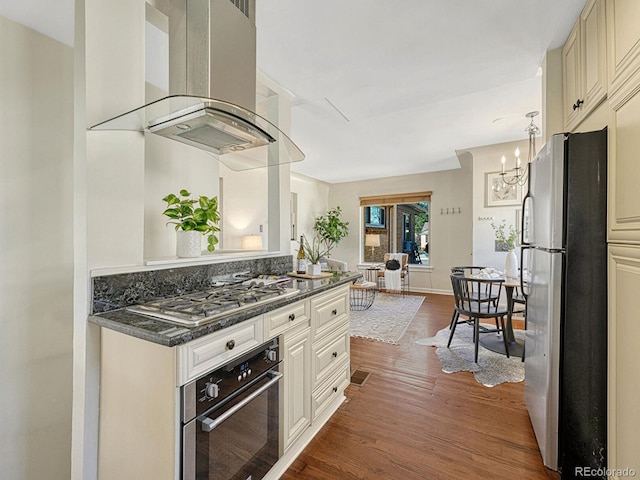 732 Poplar St, Denver, CO 80220 - kitchen with appliances with stainless steel finishes, ventilation hood, wood finished floors, a chandelier, and cream cabinetry
