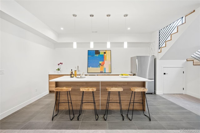 kitchen featuring stainless steel refrigerator, a center island, hanging light fixtures, tile patterned flooring, and a breakfast bar area