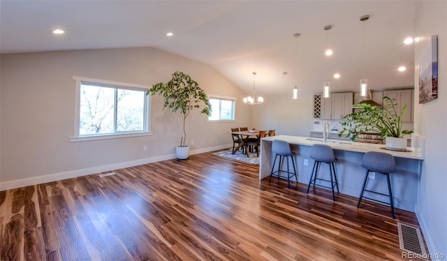 kitchen with light countertops, a breakfast bar, visible vents, wall chimney range hood, and lofted ceiling