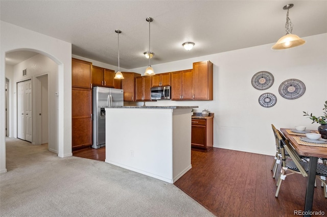 kitchen with dark colored carpet, a kitchen island, hanging light fixtures, and appliances with stainless steel finishes