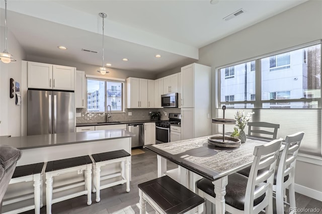 kitchen with pendant lighting, tasteful backsplash, white cabinetry, sink, and stainless steel appliances