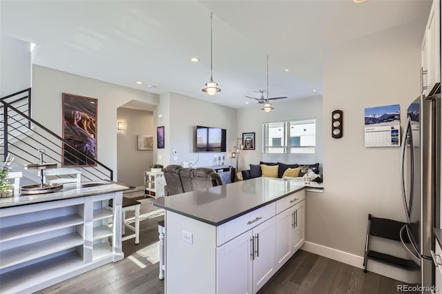 kitchen featuring dark wood-type flooring, stainless steel fridge, white cabinets, decorative light fixtures, and kitchen peninsula