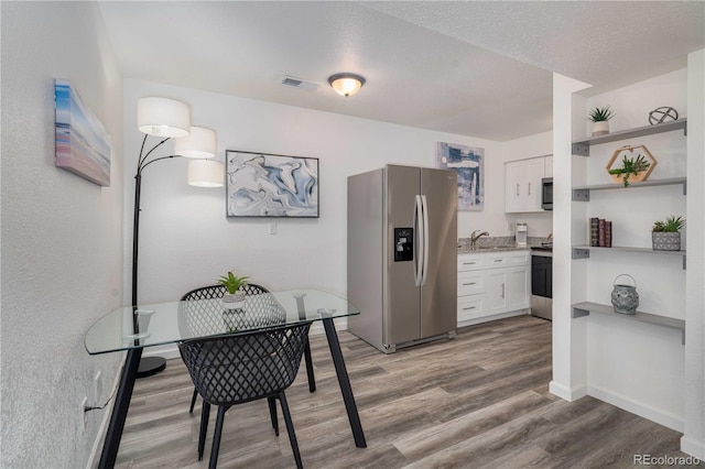 dining space with baseboards, visible vents, a textured ceiling, and light wood finished floors