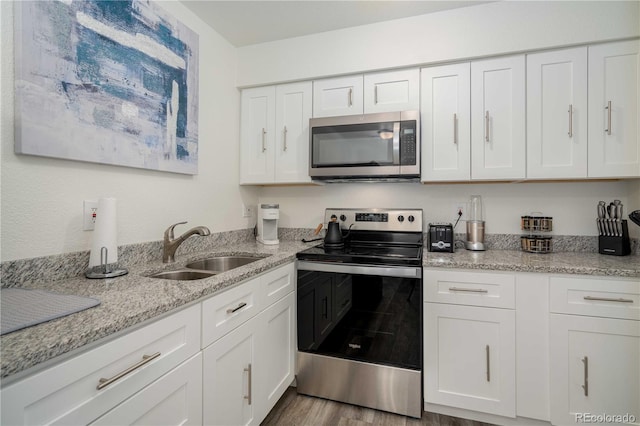 kitchen featuring light stone counters, stainless steel appliances, wood finished floors, a sink, and white cabinets