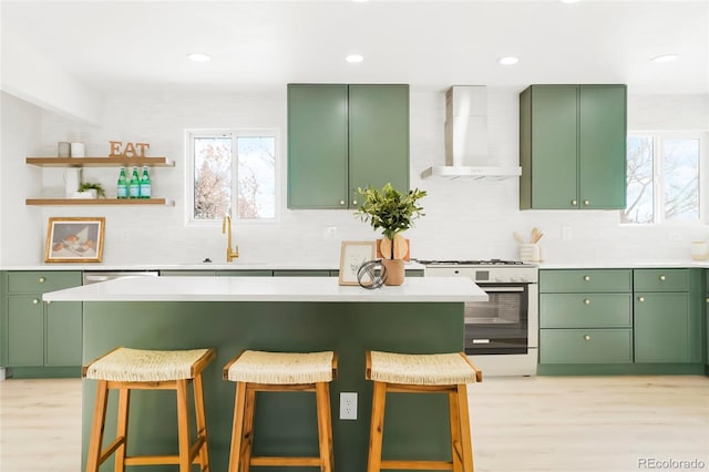 kitchen featuring a sink, a breakfast bar area, wall chimney range hood, green cabinetry, and white range with gas stovetop