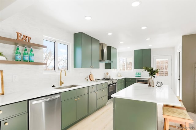 kitchen featuring range with gas cooktop, wall chimney range hood, green cabinetry, stainless steel dishwasher, and a sink