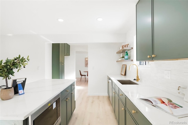 kitchen featuring open shelves, a sink, backsplash, light wood-style floors, and green cabinetry