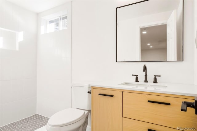 bathroom with a tile shower, toilet, and vanity