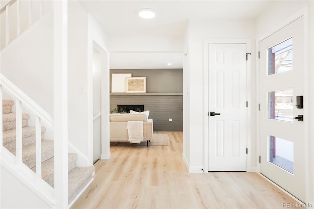 foyer featuring baseboards, a fireplace, wood finished floors, and stairs