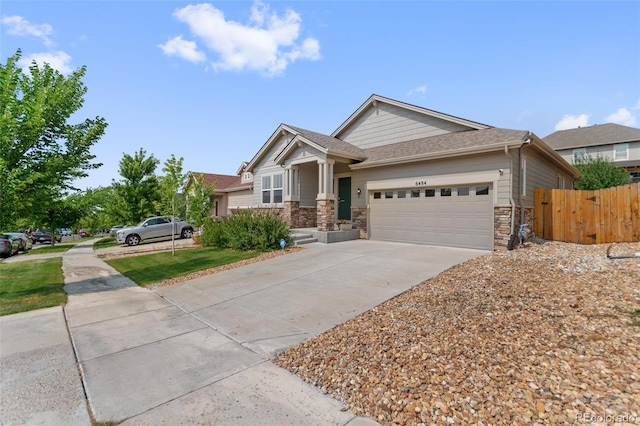 craftsman inspired home featuring a garage, concrete driveway, stone siding, and fence