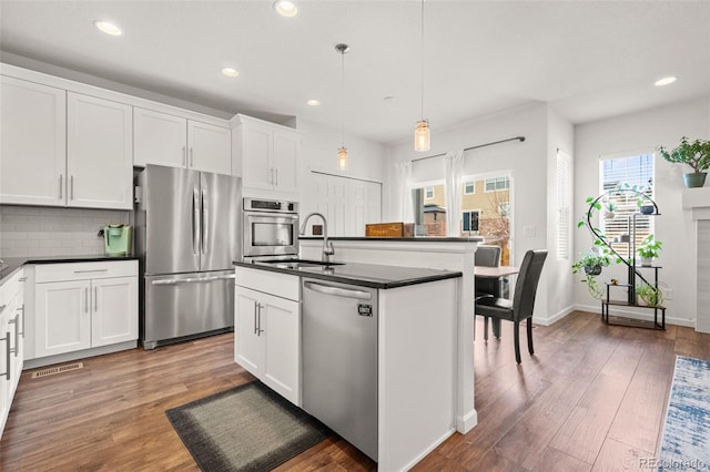 kitchen featuring white cabinetry, decorative light fixtures, a center island with sink, appliances with stainless steel finishes, and dark hardwood / wood-style flooring