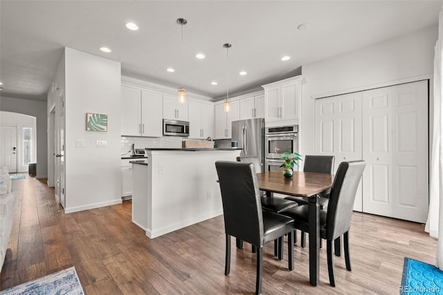 dining area featuring light wood-style floors, arched walkways, baseboards, and recessed lighting