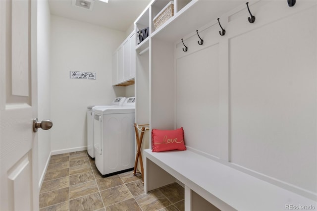 clothes washing area with washer and dryer, stone finish floor, cabinet space, and baseboards