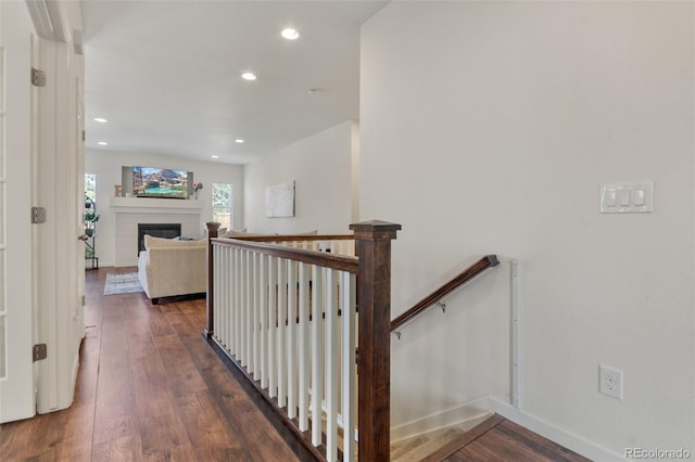 hall featuring recessed lighting, baseboards, dark wood-style flooring, and an upstairs landing