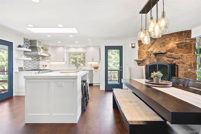 2976 Hiwan Dr, Evergreen, CO 80439 - kitchen featuring wall chimney range hood, light countertops, white cabinetry, a center island, and a stone fireplace