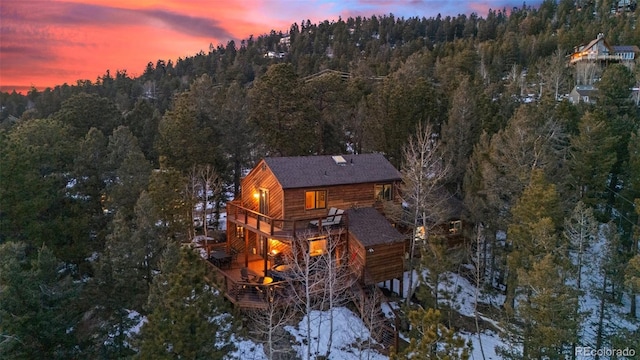 back of property at dusk with a deck and a view of trees