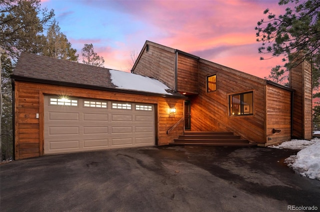 view of front of home with driveway, an attached garage, a chimney, and roof with shingles