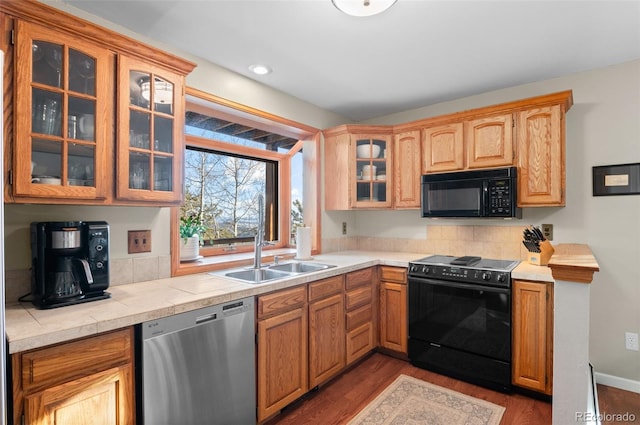 kitchen featuring glass insert cabinets, dark wood finished floors, a sink, and black appliances