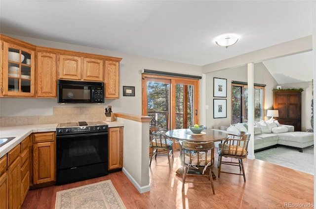 kitchen with glass insert cabinets, open floor plan, light countertops, light wood-type flooring, and black appliances