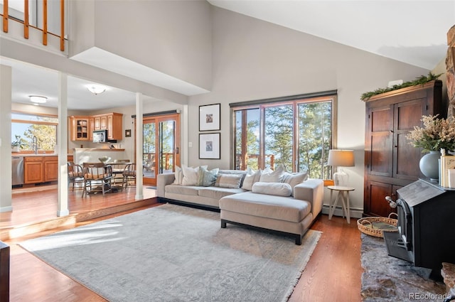 living room featuring a baseboard heating unit, a healthy amount of sunlight, high vaulted ceiling, and wood finished floors