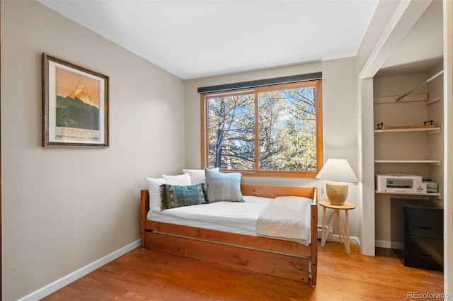 bedroom featuring a baseboard heating unit, baseboards, and wood finished floors