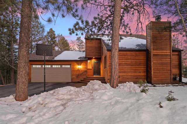 chalet / cabin featuring a garage, driveway, and a chimney