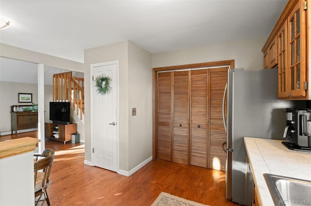 kitchen featuring baseboards, brown cabinetry, tile countertops, glass insert cabinets, and dark wood-style flooring